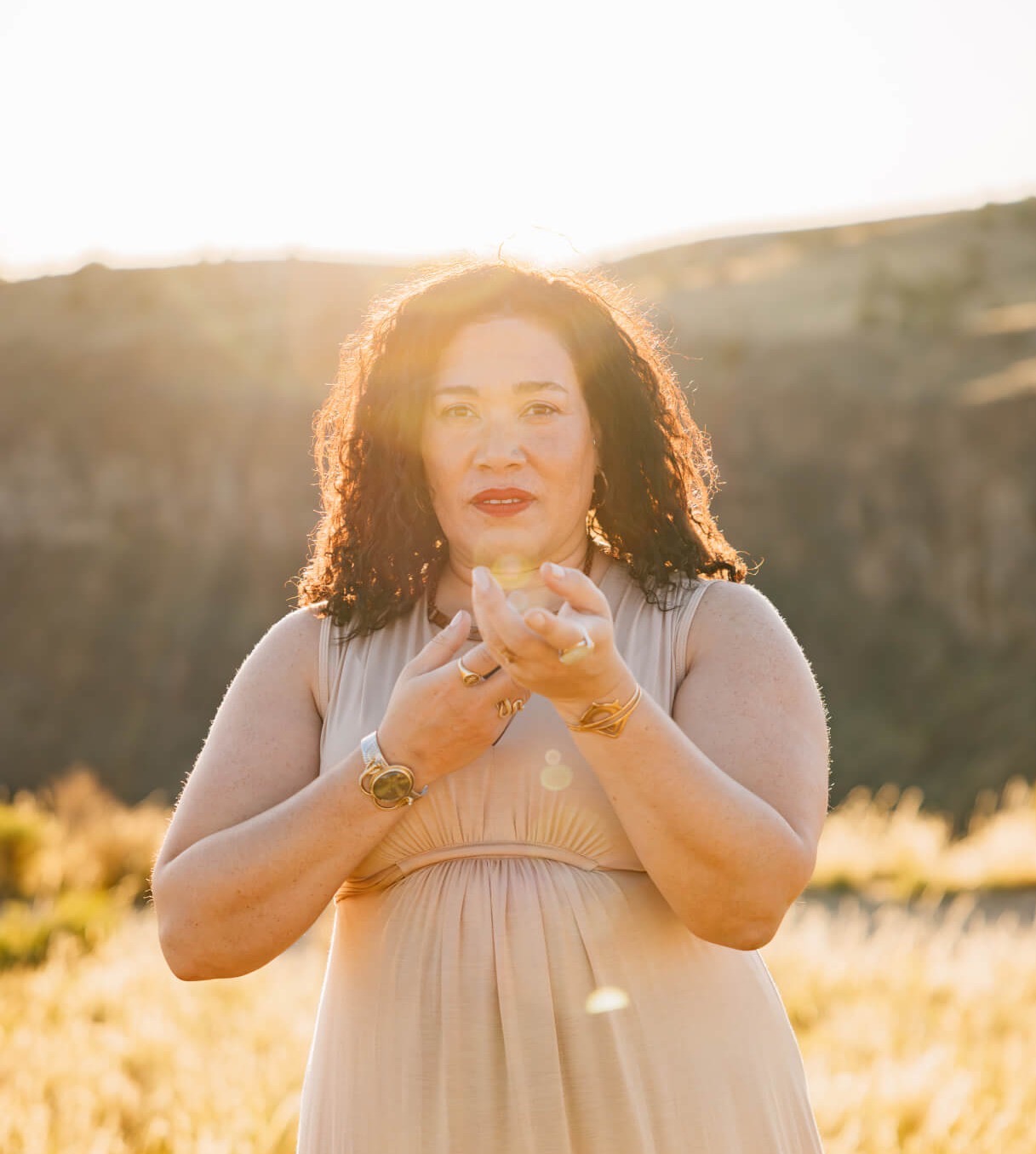 Elisha standing on an open plain of grass, using her hands to call in energy. The sun is setting behind her